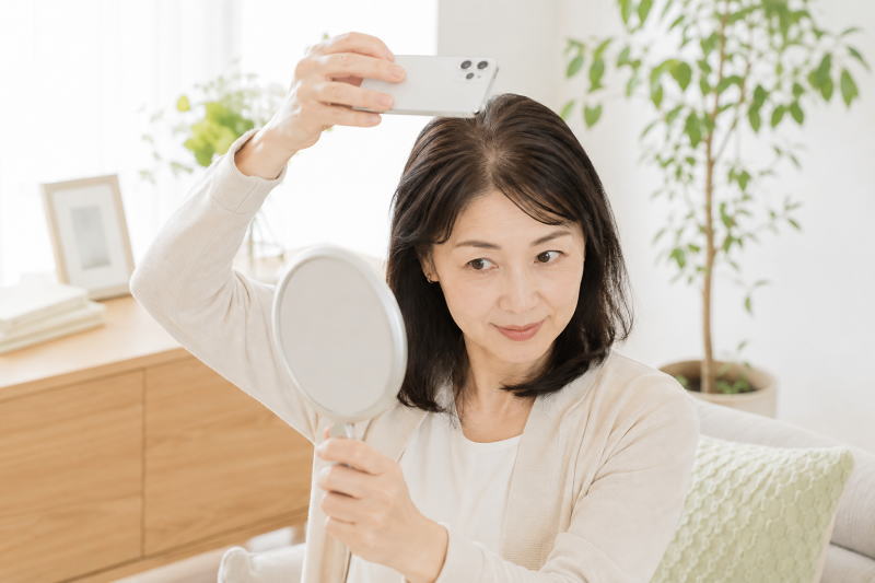 女性が手鏡やスマートフォンを使い、髪の状態を穏やかに確認している場面